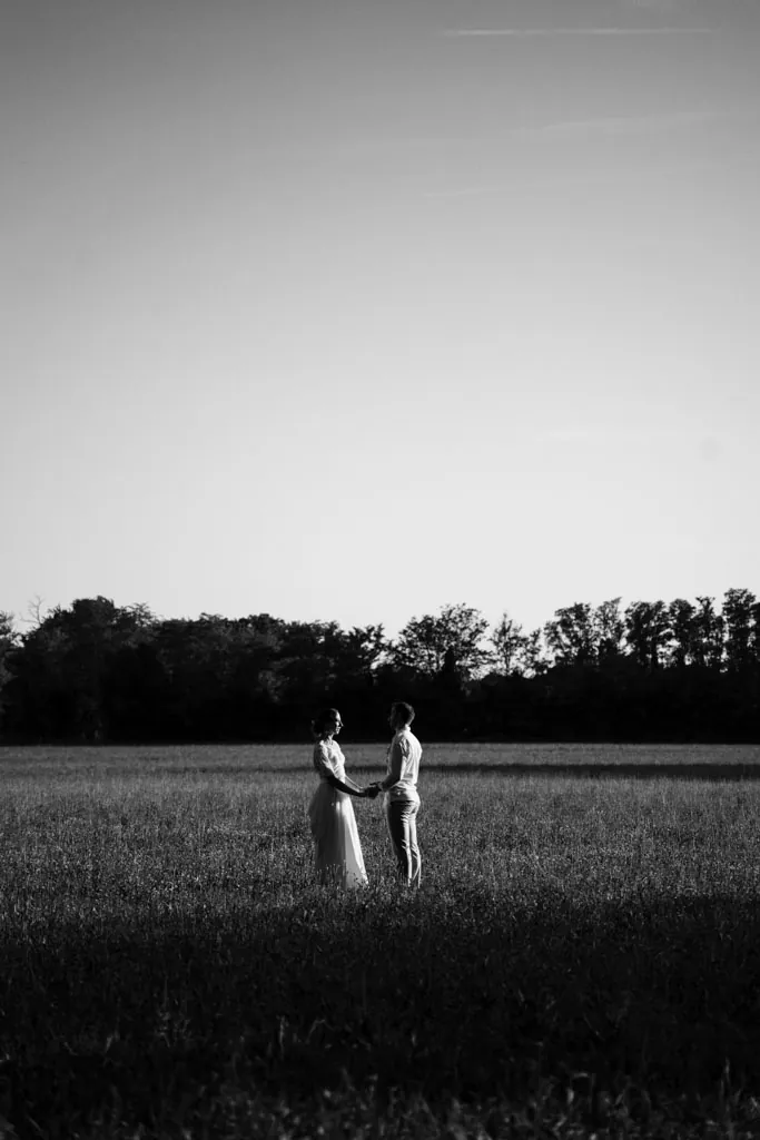 Couple de mariés au loin dans un champ, photographie en noir et blanc