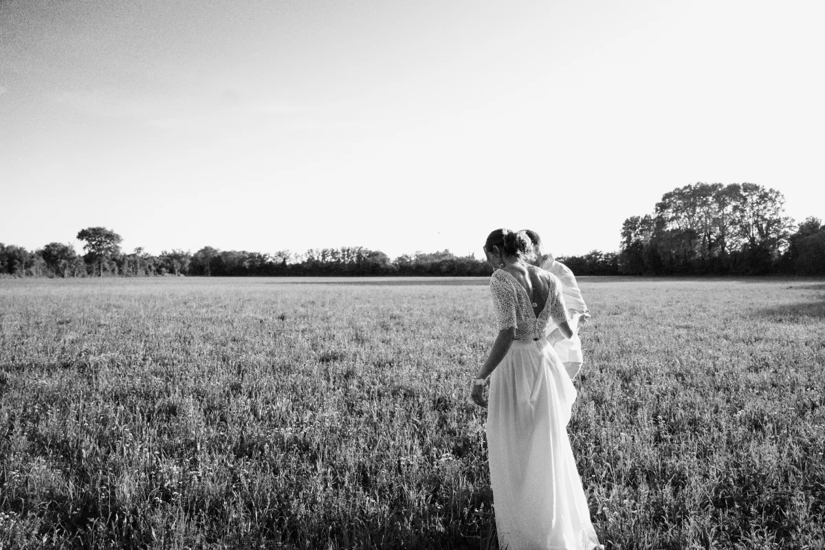 Mariée de dos dans un champ de hautes herbes, photographie en noir et blanc
